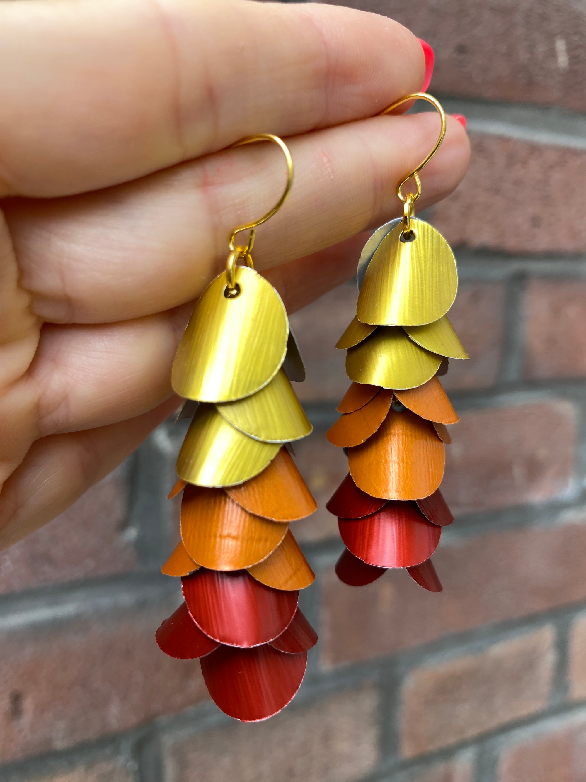 Colorful layered earrings made from upcycled nespresso capsules  held by a hand against a brick wall background