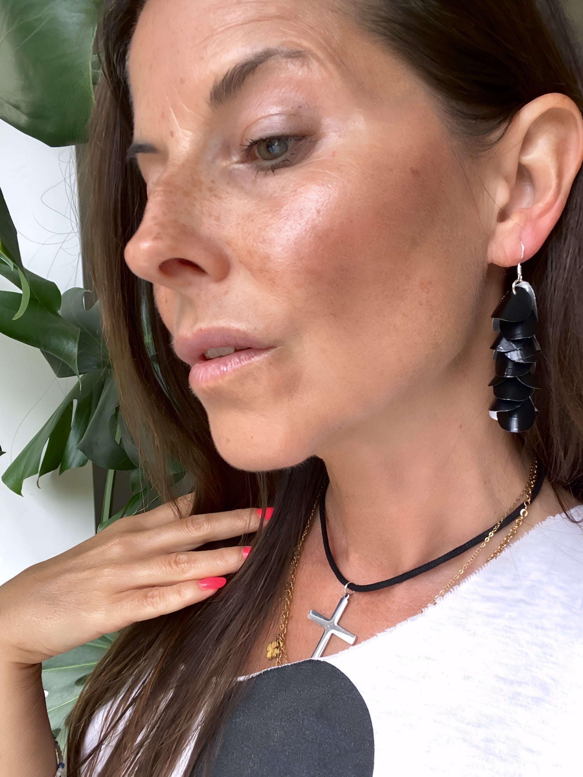 Woman wearing black earrings made from upcycled nespresso capsules with green leaves in the background.