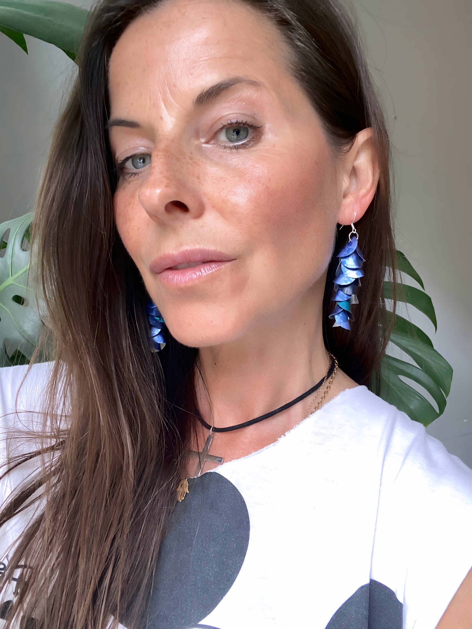 women wears blue cascade earrings made from upcycled nespresso pods against a neutral wall background