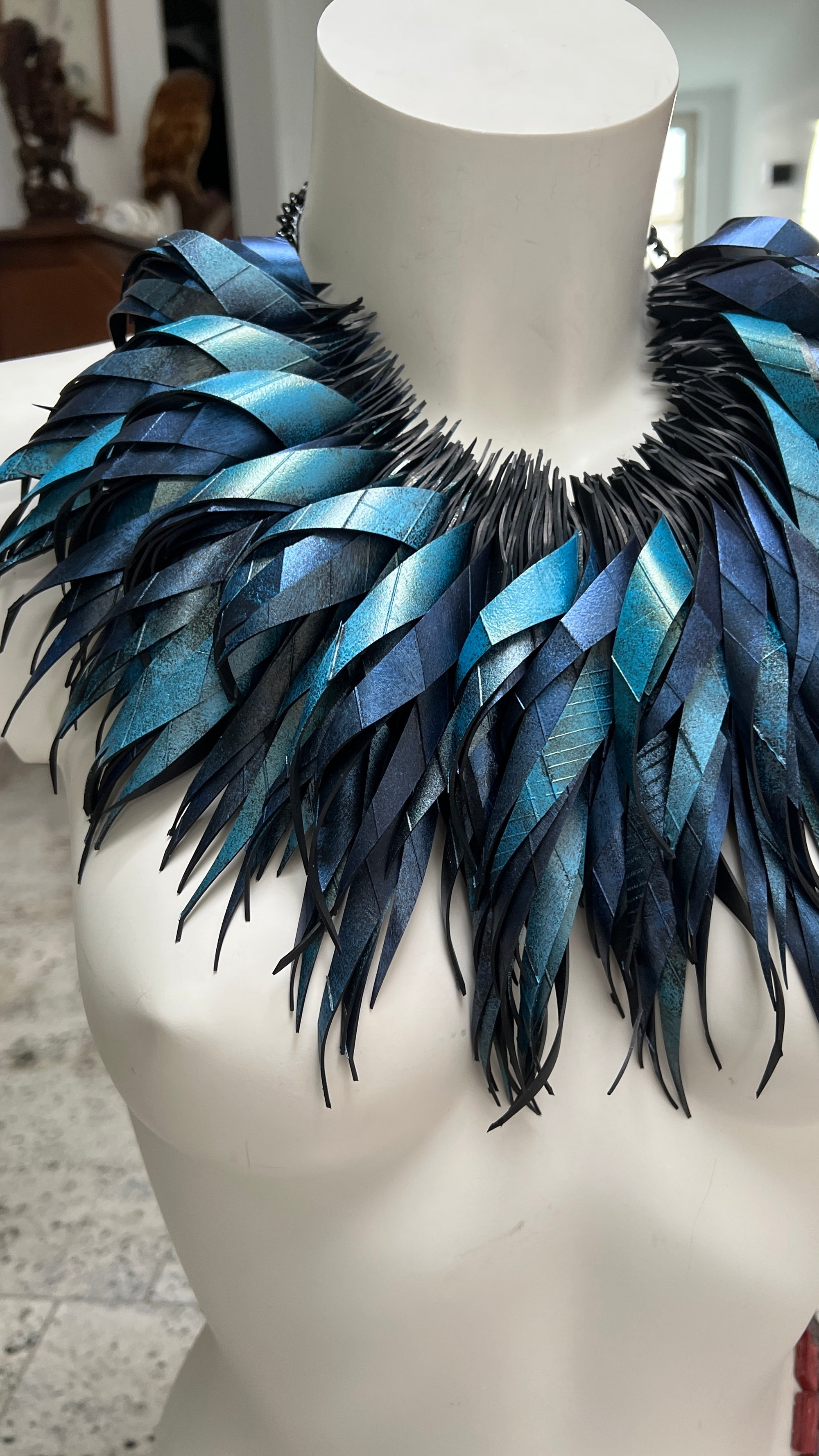 metallic bue coloured large, chunky curly tassel necklace made from upcycled bicycle inner tube on a white mannequin in  a luxurious home environment 