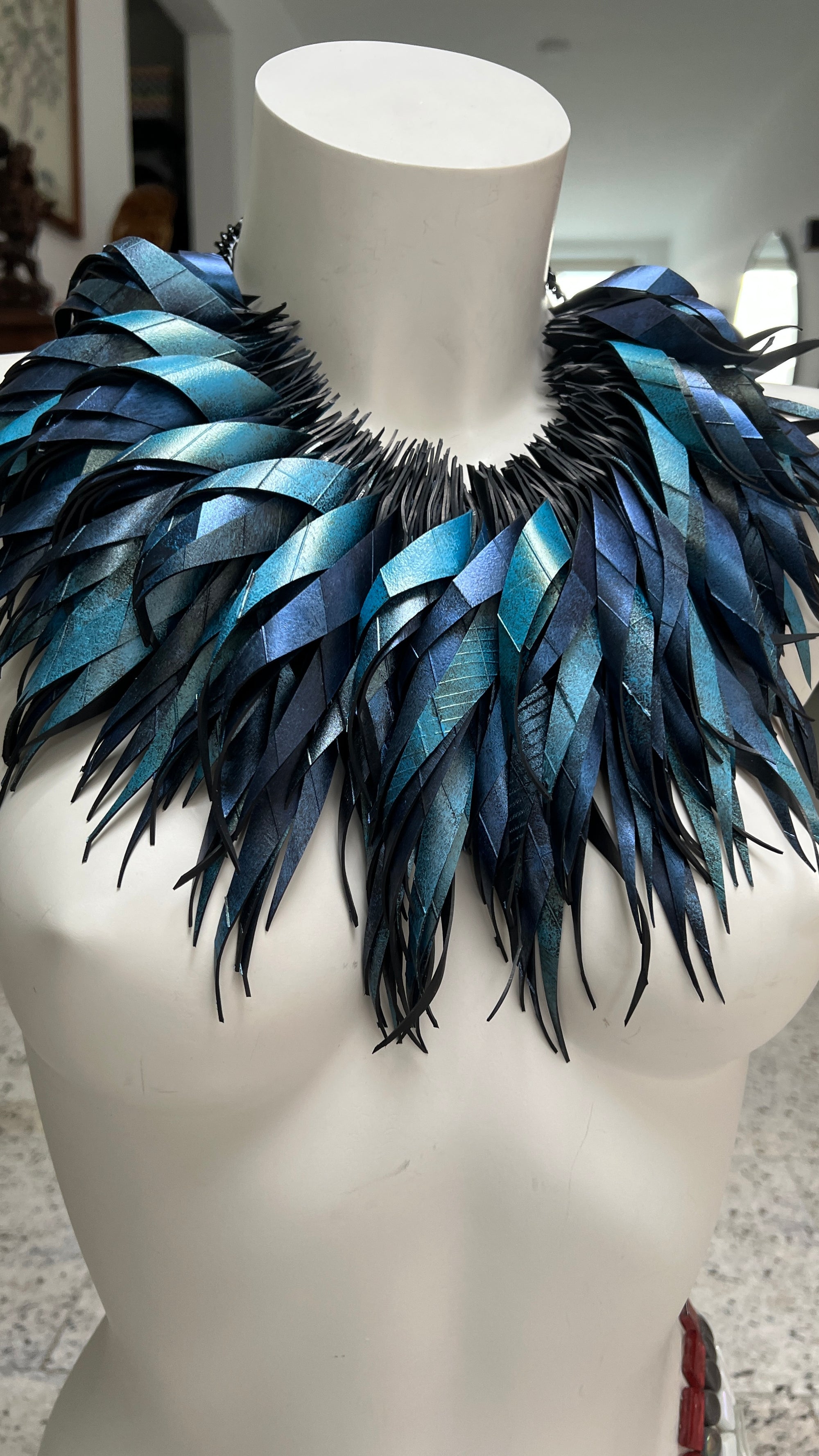 metallic bue coloured large, chunky curly tassel necklace made from upcycled bicycle inner tube on a white mannequin in  a luxurious home environment 