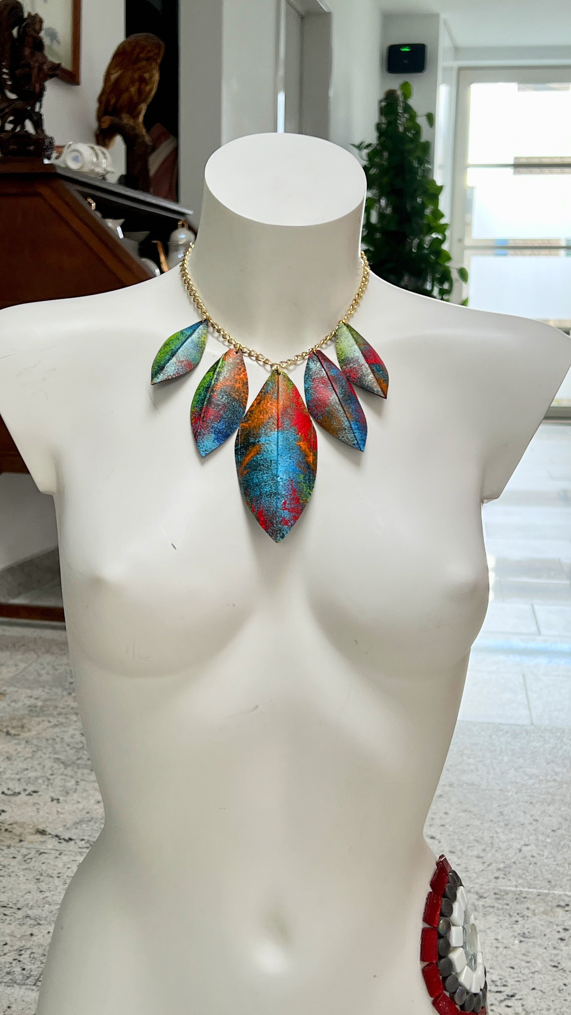 Colorful leaf-style necklace made from upcycled bicycle inner tube rubber on a mannequin bust with a blurred indoor background