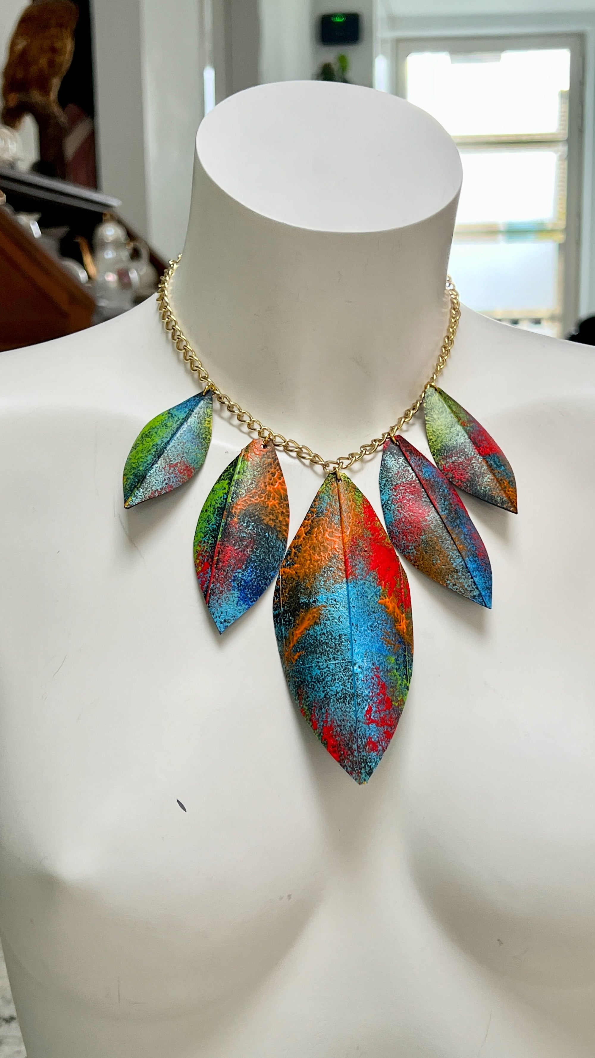 Colorful leaf-shaped necklace made from upcycled bicycle inner tube rubber on a mannequin with a blurred indoor background