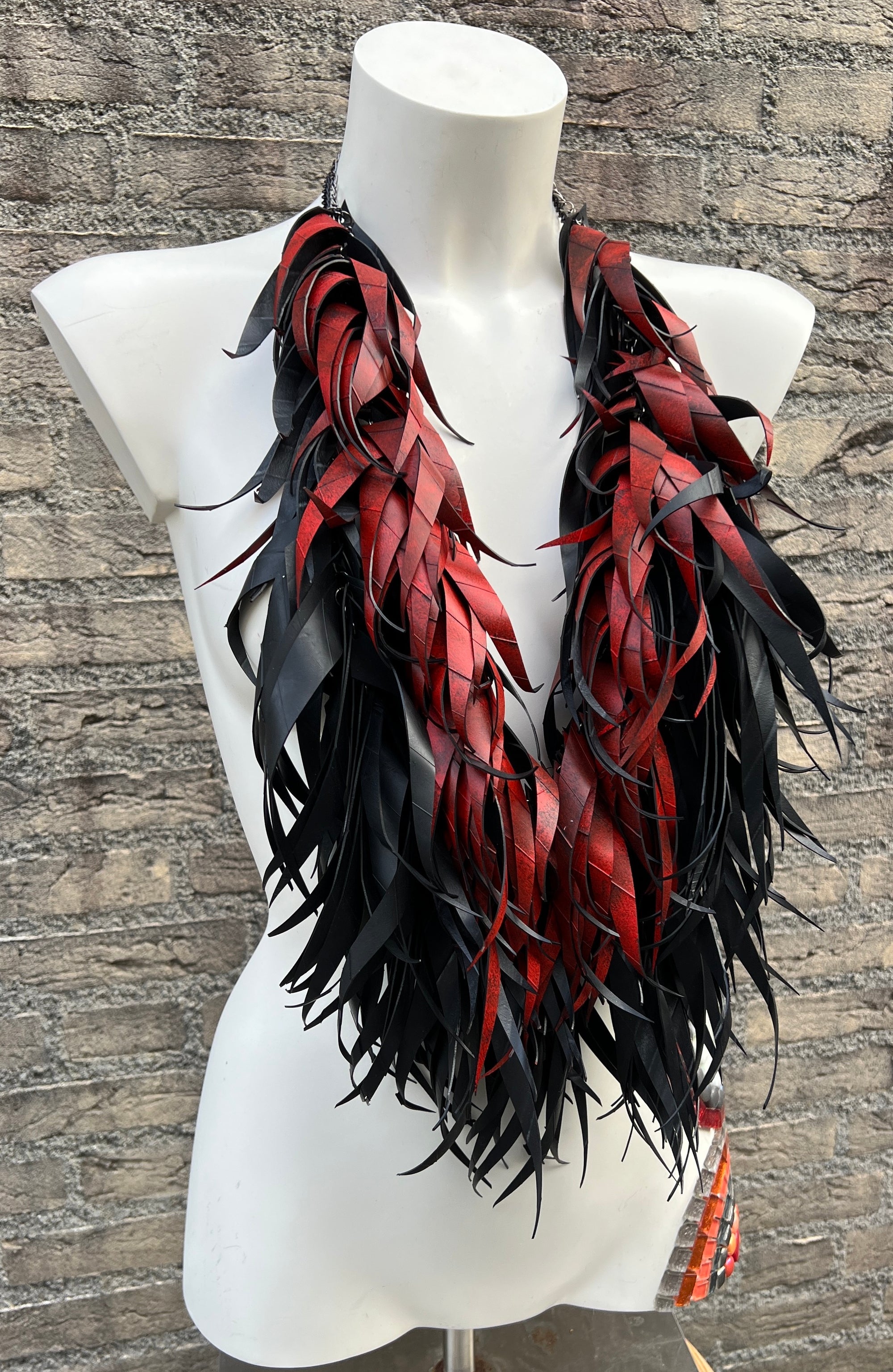 mannequin wearing red and black curly tassel necklace  made from upcycled bicycle inner tubes against a brick wall