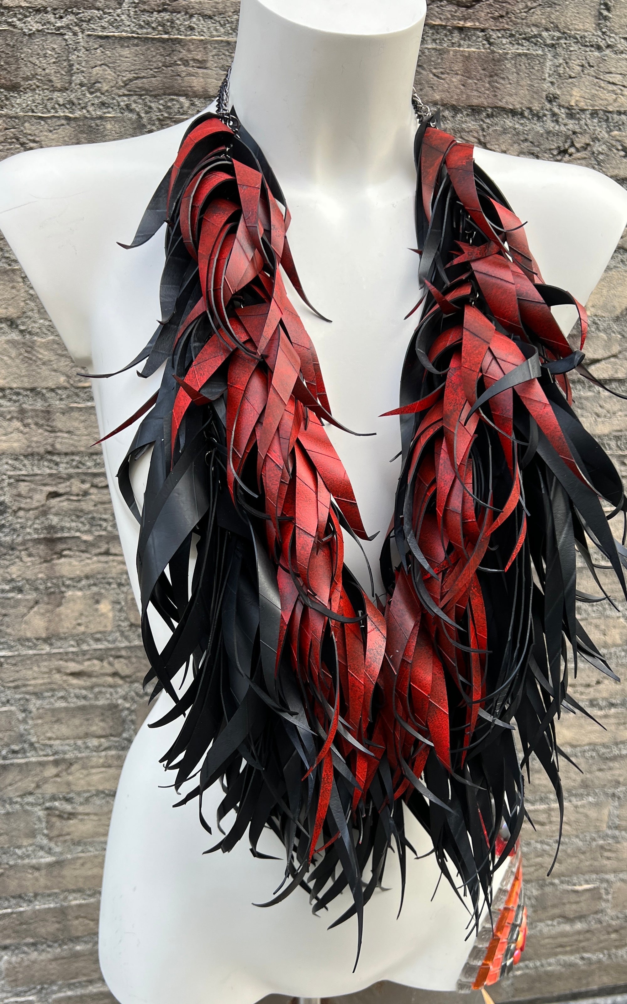 Black and red curly tassel necklace made from upcycled bicycle tyre rubber  on a mannequin against a stone wall background