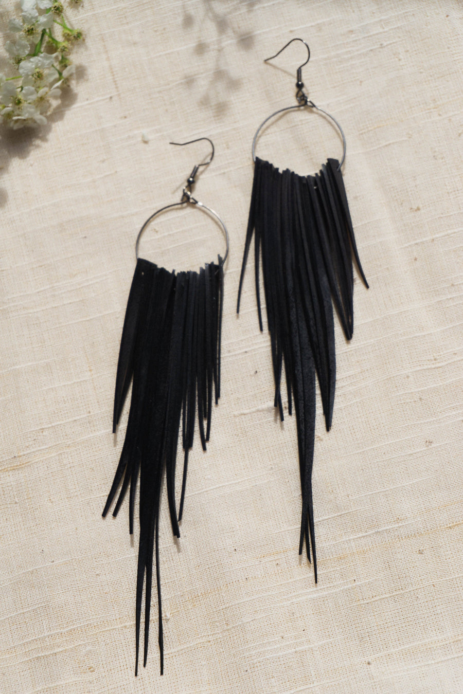 long, upcycled, black coloured, bicycle inner tube tassel earrings on a light fabric background