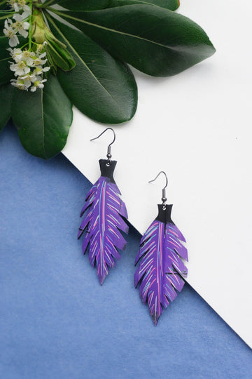 Leaf shaped purple coloured earrings made from upcycled bicycle inner tube rubber on blue and white background and a plant