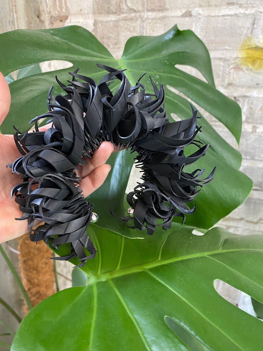 chunky large curly black bracelet made from upcycled bicycle innertube tyre in front of a large plant