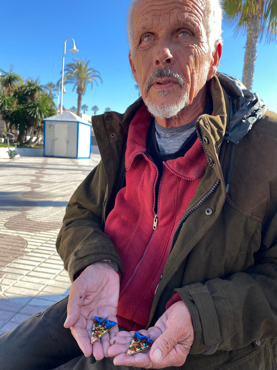 man holds artistic square statement earrings in blue, yellow and red colours made from upcycled bicycle inner tube and cork