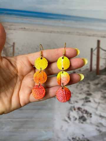 delicate sunrise sunset themed earrings made from upcycled bicycle inner tubes, yellow orange earrings with a beach background