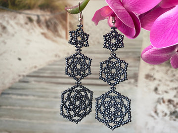 Gunmetal, metallic finish beaded earrings, with a triple floral design in front of a beach