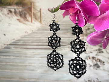 black bold beaded earrings with triple flower in front of a beach