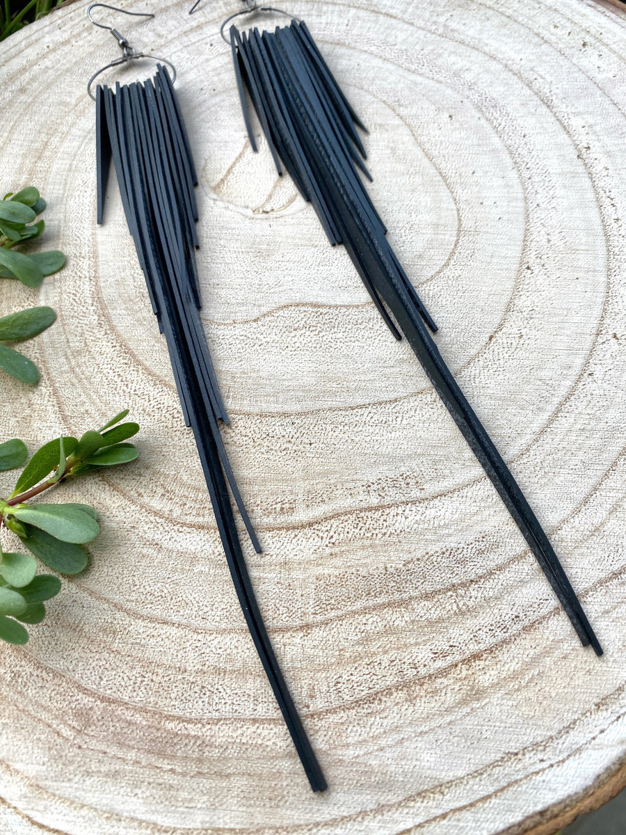 long, upcycled, black coloured, bicycle inner tube tassel earrings on a wooden background