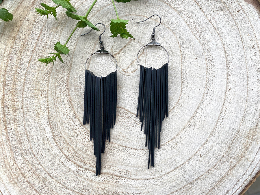 long, upcycled, black coloured, bicycle inner tube tassel earrings on a wooden background