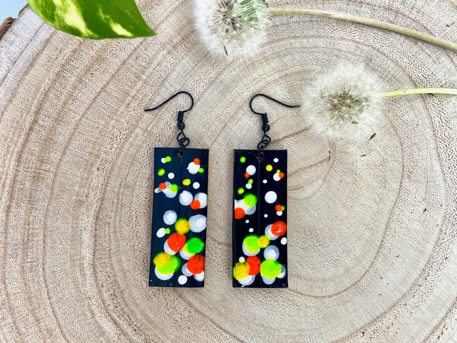 Squared-shaped earrings with black, white, orange, and yellow, green bubble design, made from upcycled bicycle inner tube on a wooden background