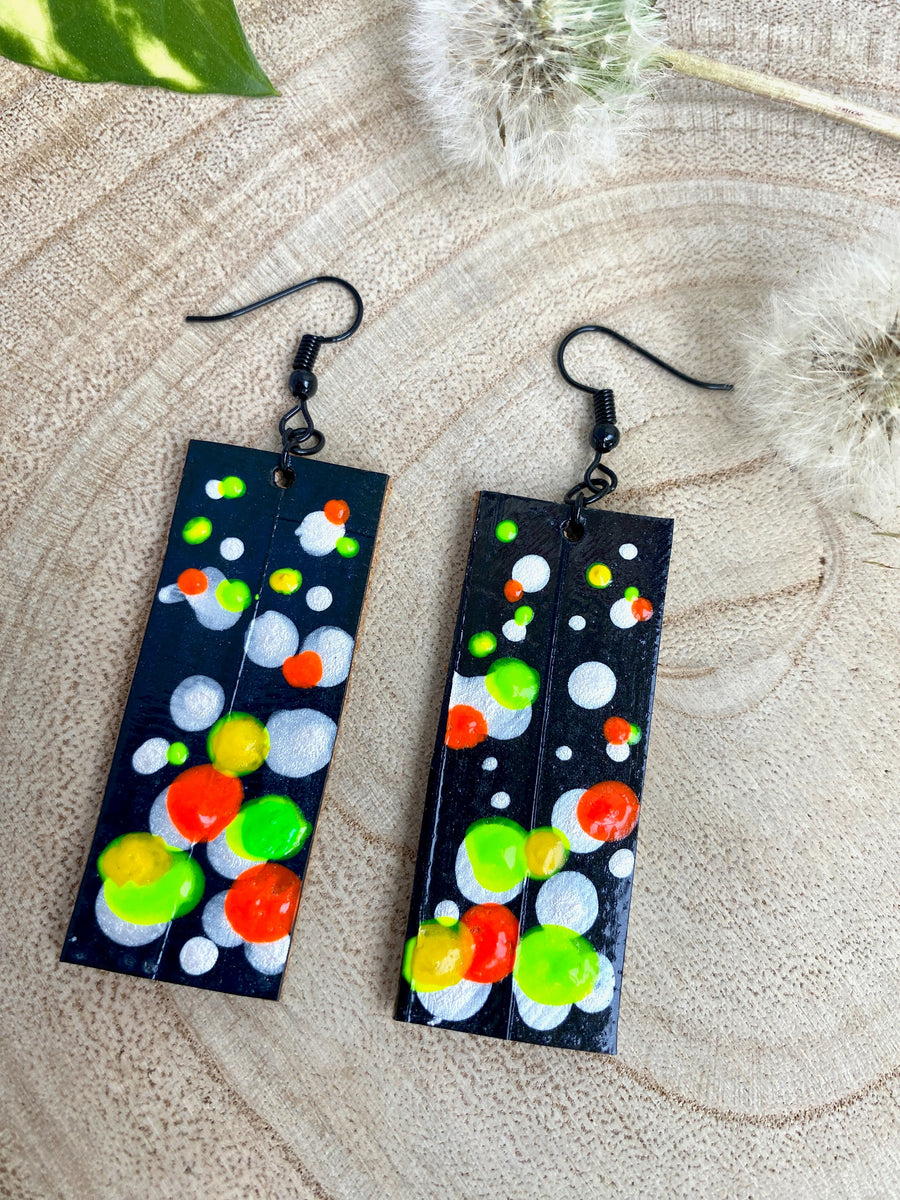 Squared-shaped earrings with black, white, orange, and yellow, green bubble design, made from upcycled bicycle inner tube on a wooden background