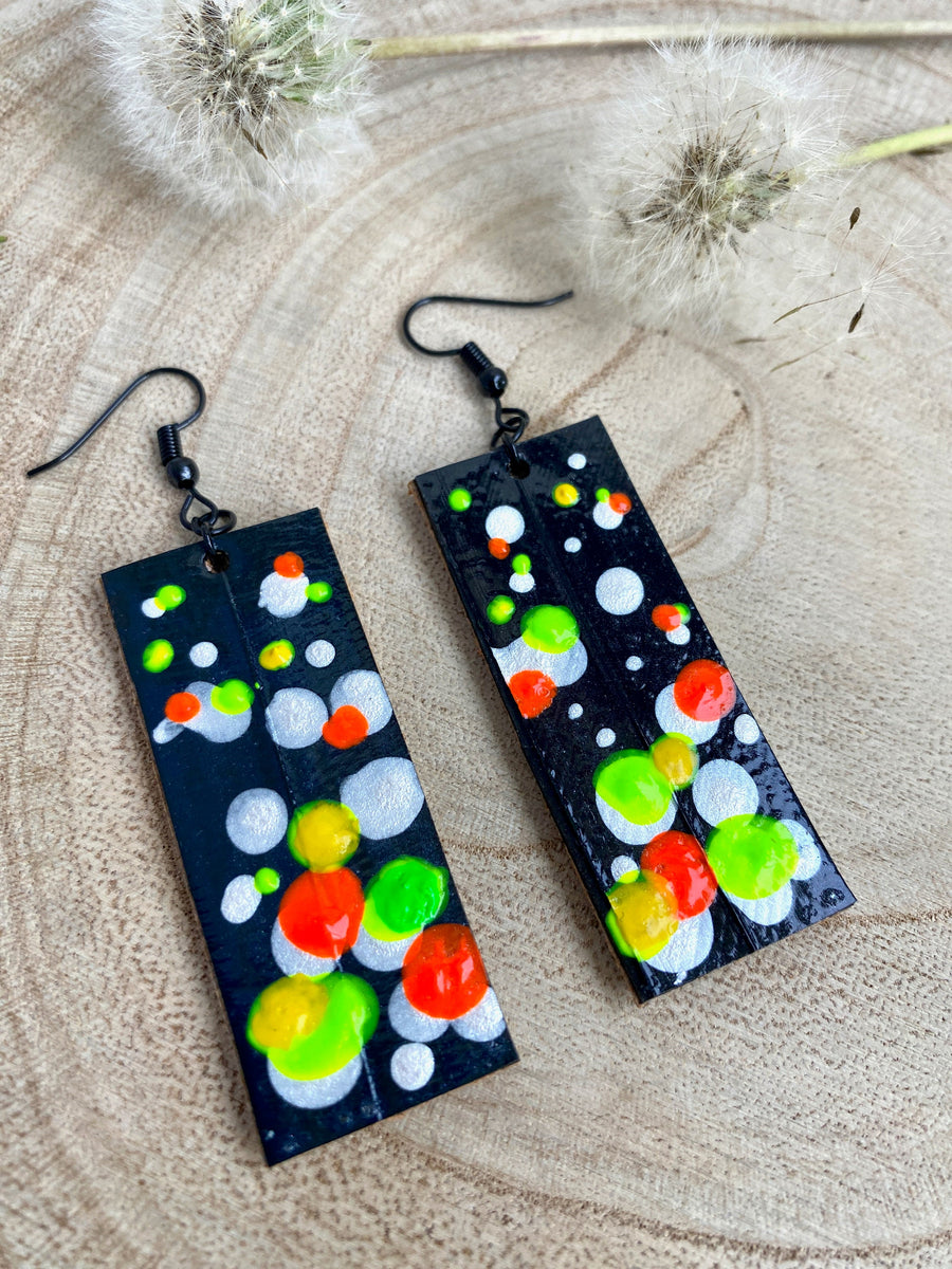 Squared-shaped earrings with black, white, orange, and yellow, green bubble design, made from upcycled bicycle inner tube on a wooden background