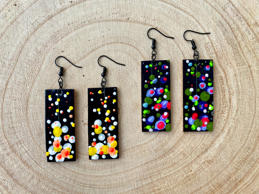 2 pairs squared-shaped earrings with black, white, orange, and yellow bubble design, made from upcycled materials on a wooden background