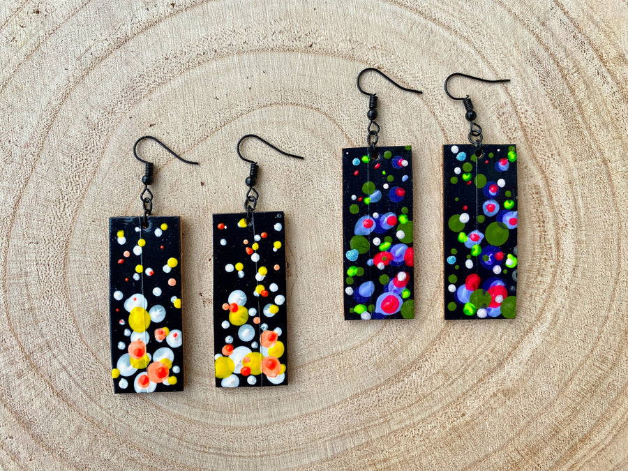 2 pairs squared-shaped earrings with black, white, orange, and yellow bubble design, made from upcycled materials on a wooden background