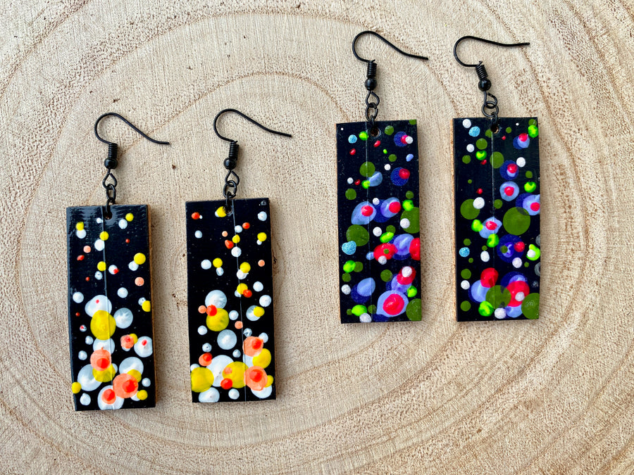 2 pairs squared-shaped earrings with black, white, orange, and yellow bubble design, made from upcycled materials on a wooden background