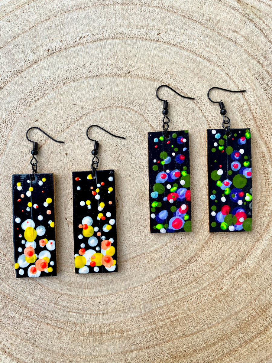 2 pairs squared-shaped earrings with black, white, orange, and yellow bubble design, made from upcycled materials on a wooden background