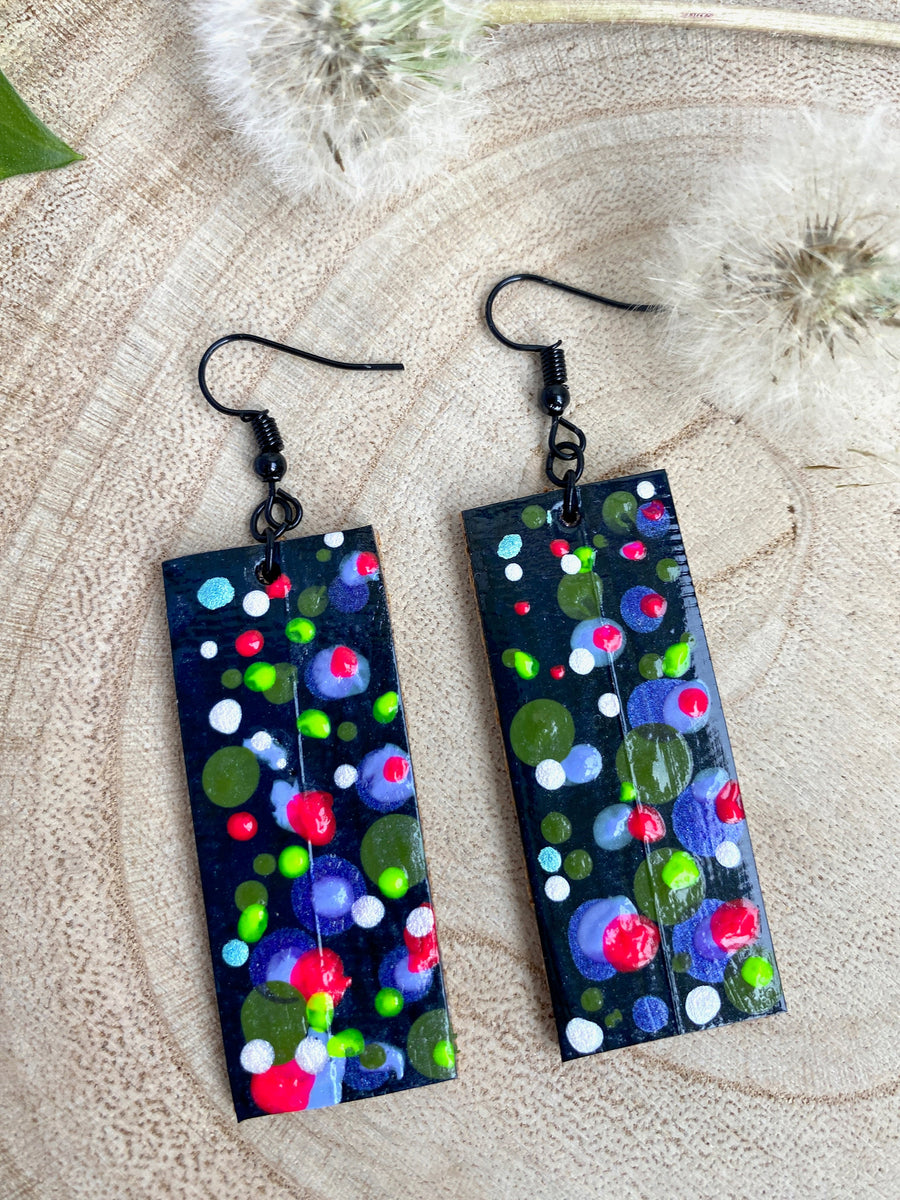 Squared-shaped earrings with black, white, orange, and yellow bubble design, made from upcycled materials on a wooden background