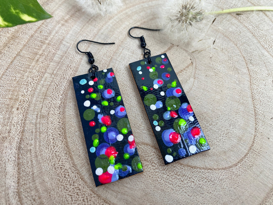 Squared-shaped earrings with black, white, orange, and yellow bubble design, made from upcycled materials on a wooden background