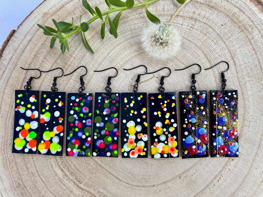 4 pairs squared-shaped earrings with black, white, orange, and yellow bubble design, made from upcycled materials on a wooden background