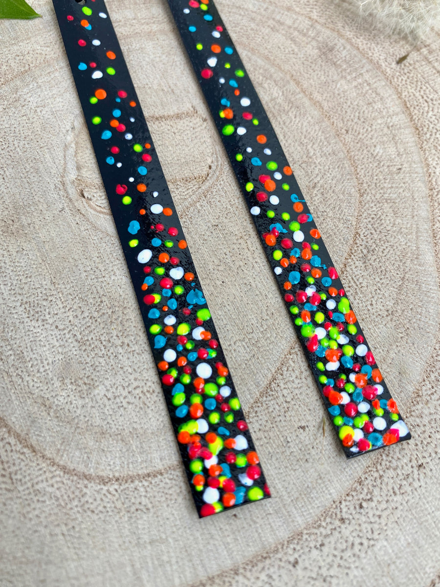 Long, black upcycled inner tube strap shaped earrings decorated with colourful polka dots, on a wooden background