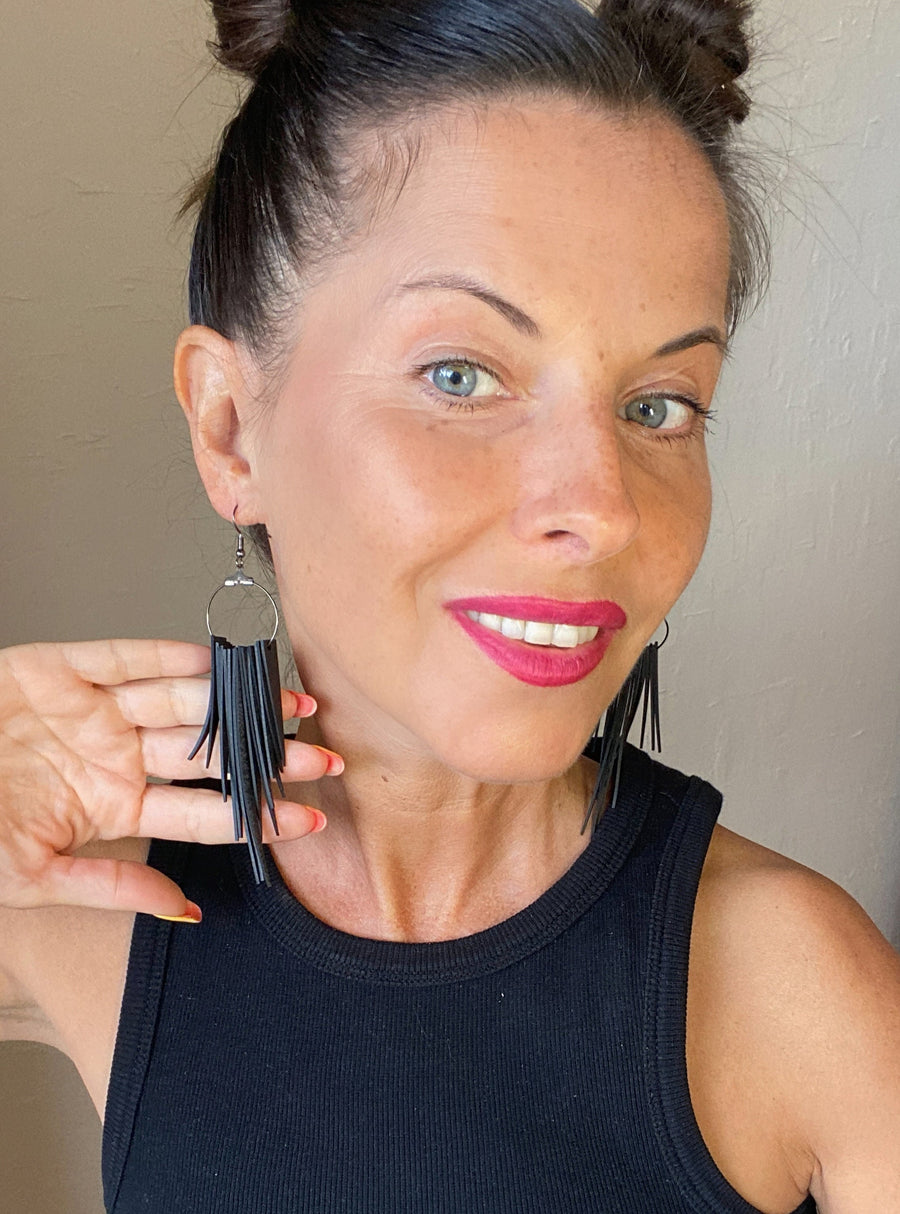 model wears long, black, upcycled bicycle inner tube tassel earrings made from bicycle tyre inner tubes on a wooden background