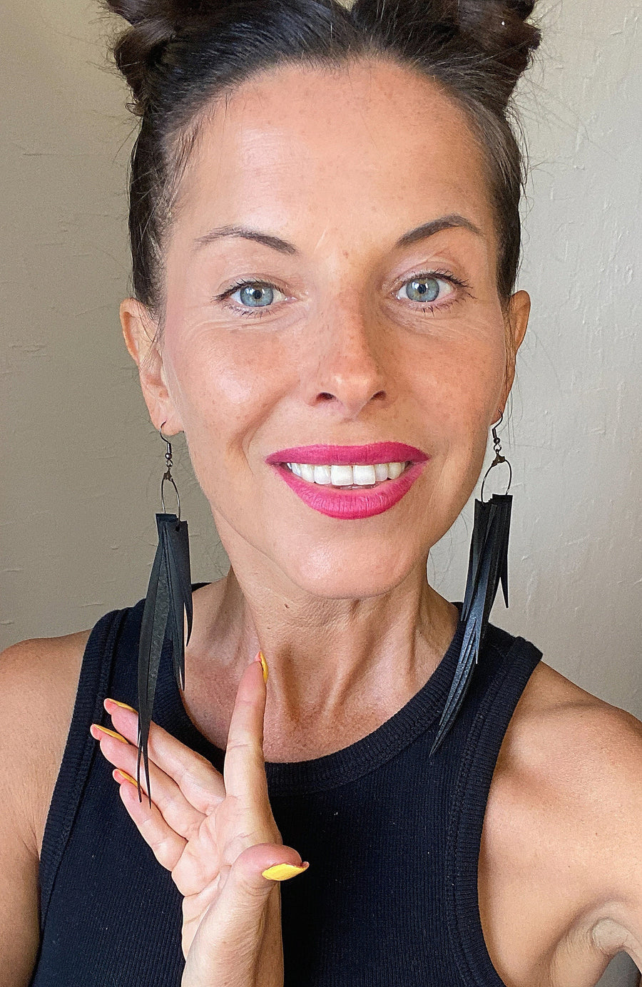 model wears long, black, upcycled bicycle inner tube tassel earrings made from bicycle tyre inner tubes on a wooden background