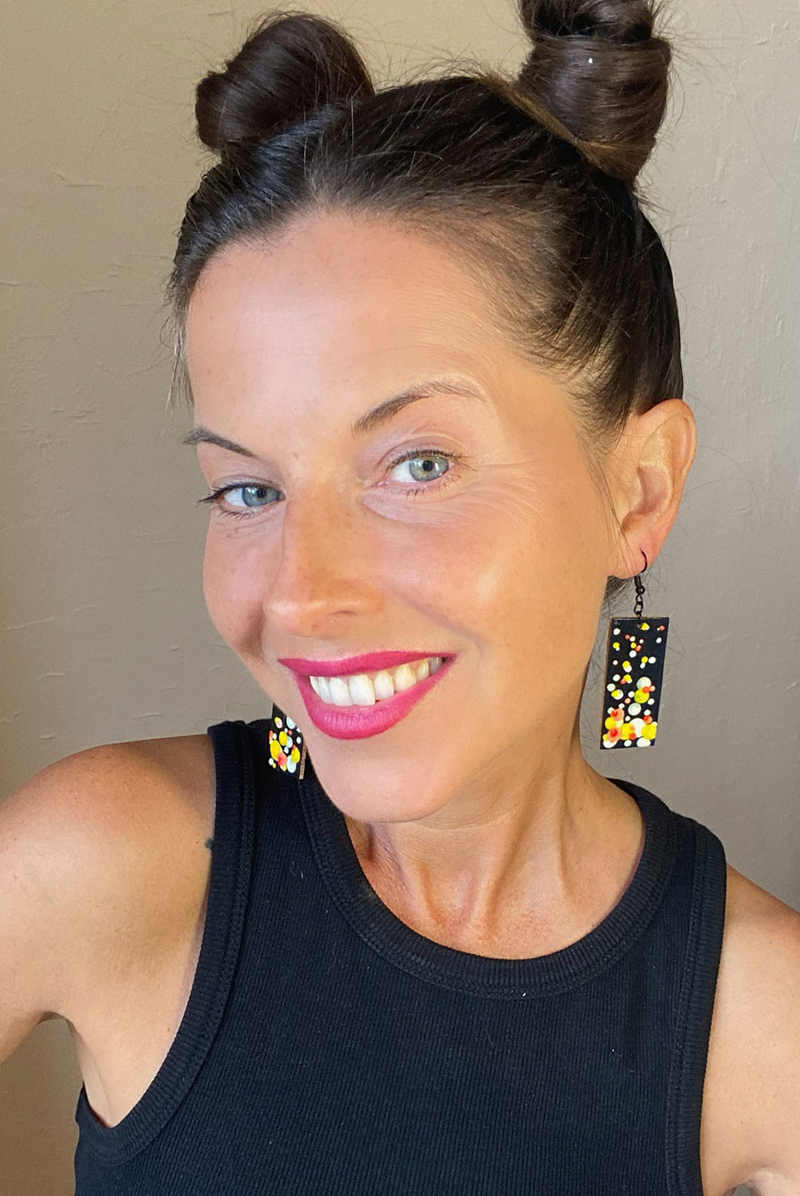 model wears Squared-shaped earrings with black, white, orange, and yellow bubble design, made from upcycled materials