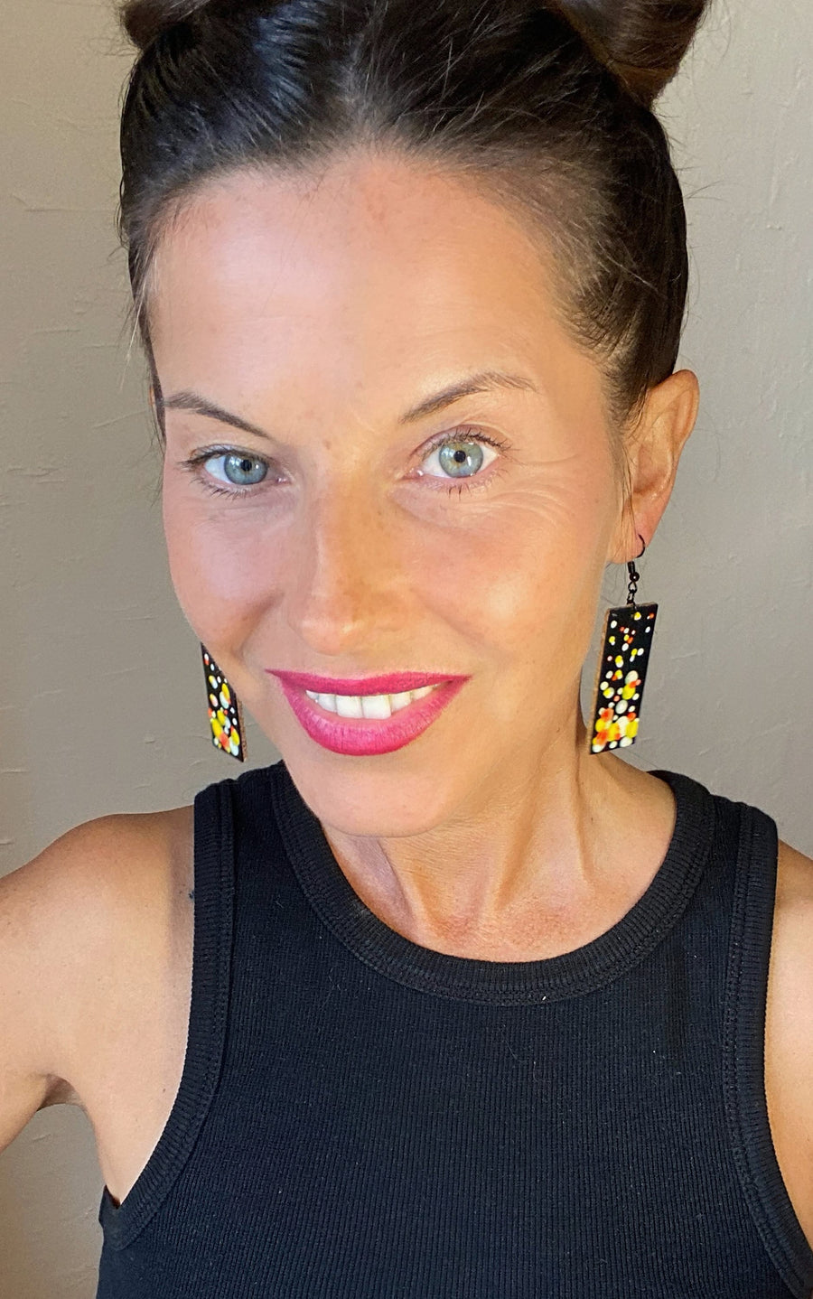 model wears Squared-shaped earrings with black, white, orange, and yellow bubble design, made from upcycled materials