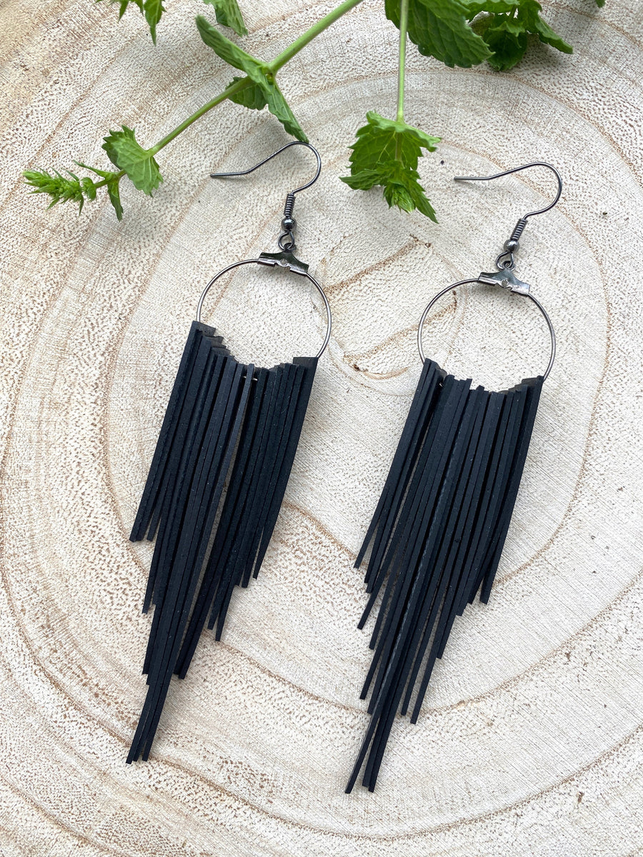 long, upcycled, black coloured, bicycle inner tube tassel earrings on a wooden background