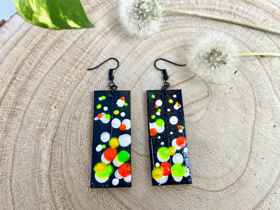 Squared-shaped earrings with black, white, orange, and yellow, green bubble design, made from upcycled bicycle inner tube on a wooden background