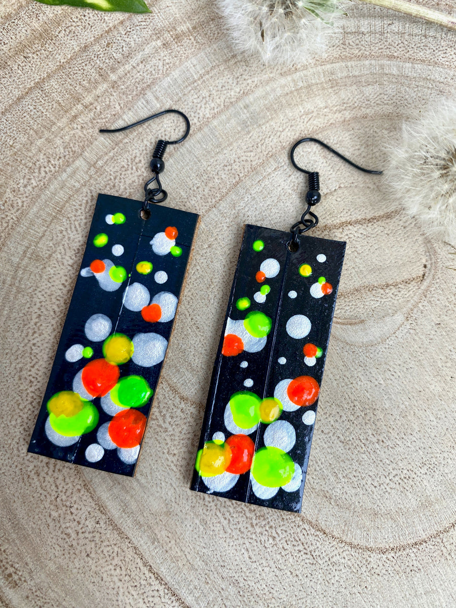 Squared-shaped earrings with black, white, orange, and yellow, green bubble design, made from upcycled bicycle inner tube on a wooden background