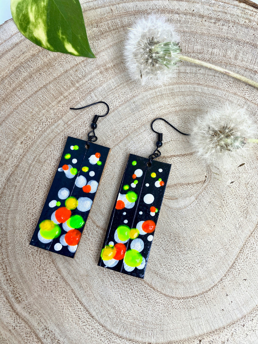 Squared-shaped earrings with black, white, orange, and yellow, green bubble design, made from upcycled bicycle inner tube on a wooden background