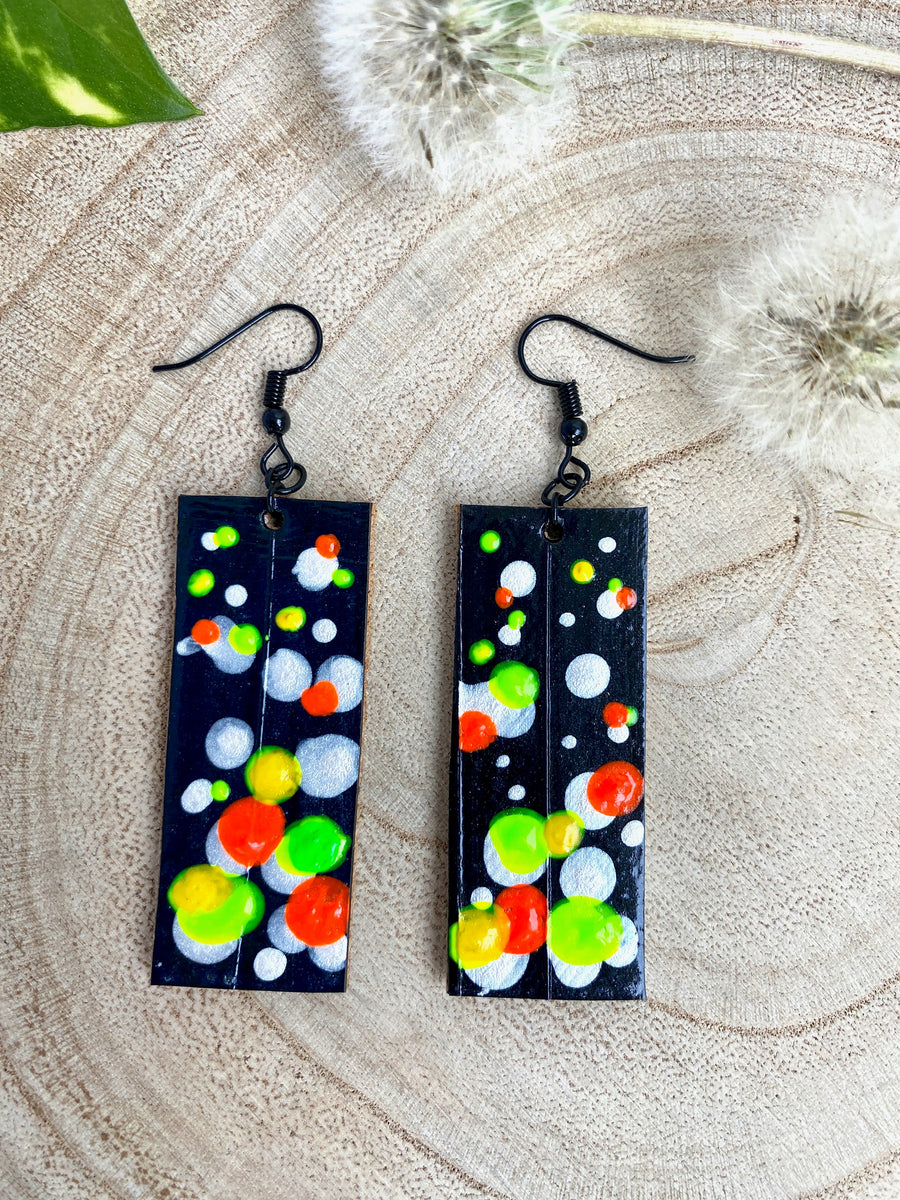 Squared-shaped earrings with black, white, orange, and yellow, green bubble design, made from upcycled bicycle inner tube on a wooden background