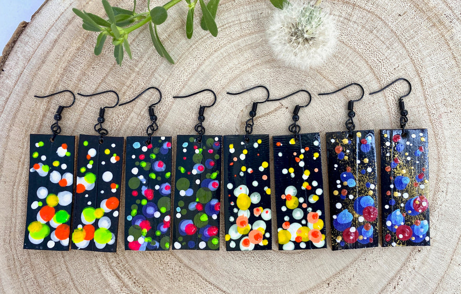 4 pairs squared-shaped earrings with black, white, orange, and yellow bubble design, made from upcycled materials on a wooden background