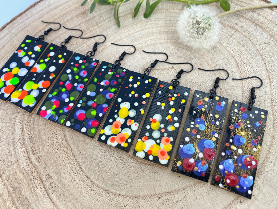 4 pairs squared-shaped earrings with black, white, orange, and yellow bubble design, made from upcycled materials on a wooden background