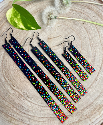 3 pairs of black upcycled bike inner tube earrings decorated with colourful polka dots on a wooden background with 2 dandelions