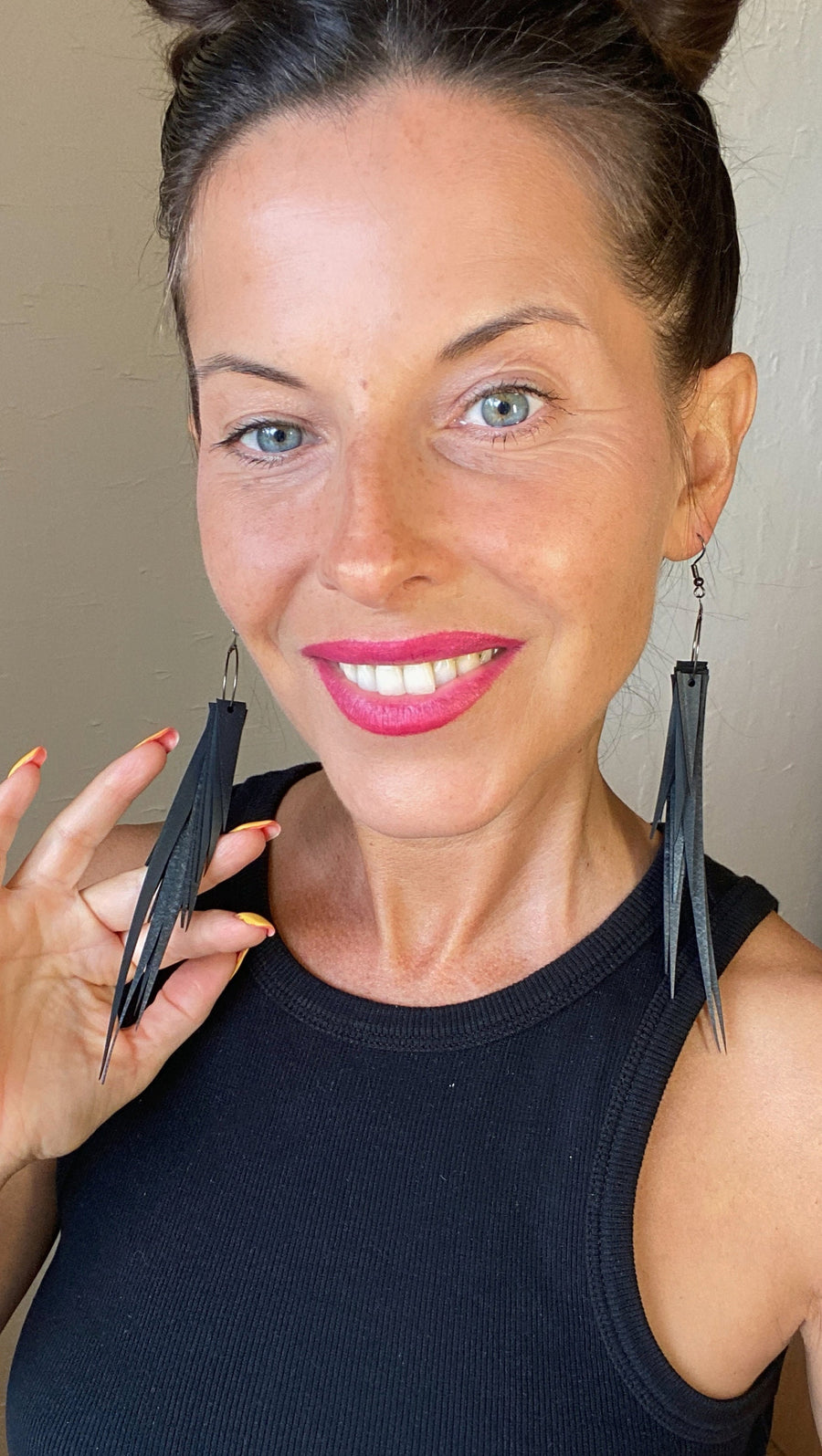 model wears long, black, upcycled bicycle inner tube tassel earrings made from bicycle tyre inner tubes on a wooden background