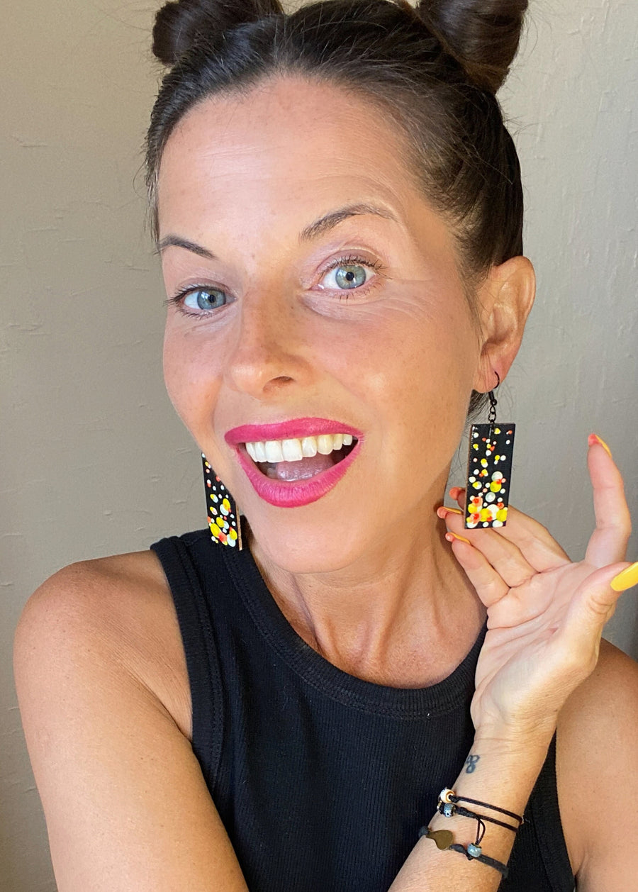 model wears Squared-shaped earrings with black, white, orange, and yellow bubble design, made from upcycled materials