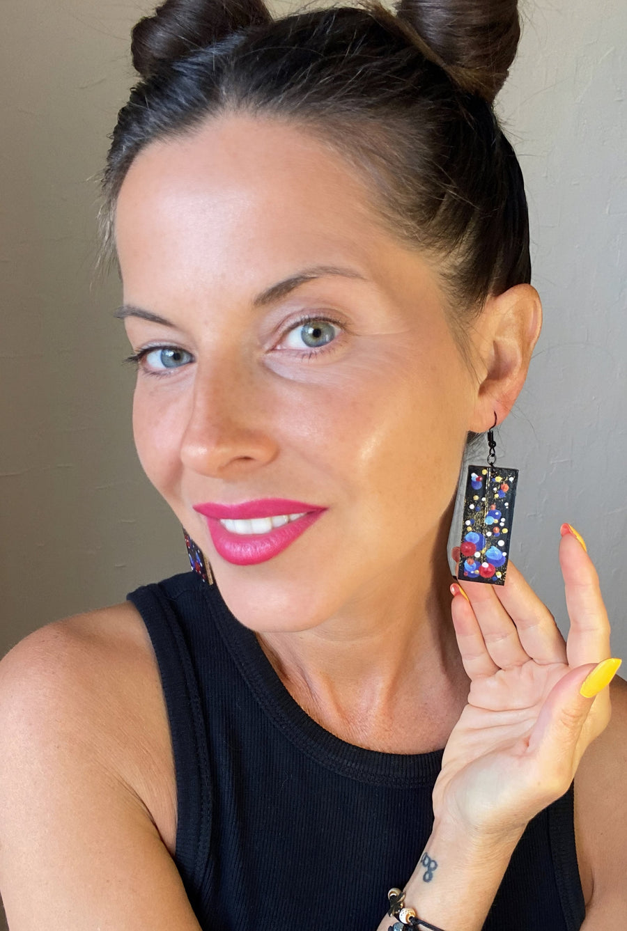 model wears squared, black earrings with blue, red, golden and silver polka dots made from scrap bicycle inner tube rubber