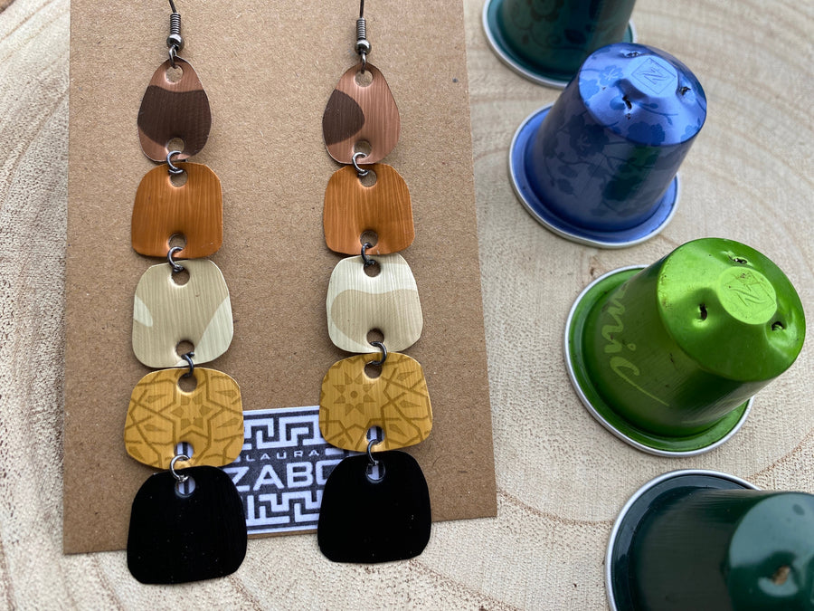 earthy coloured, brown black gold long earrings made from upcycled nespresso capsules on a wooden background, decorated with some whole nespresso capsules