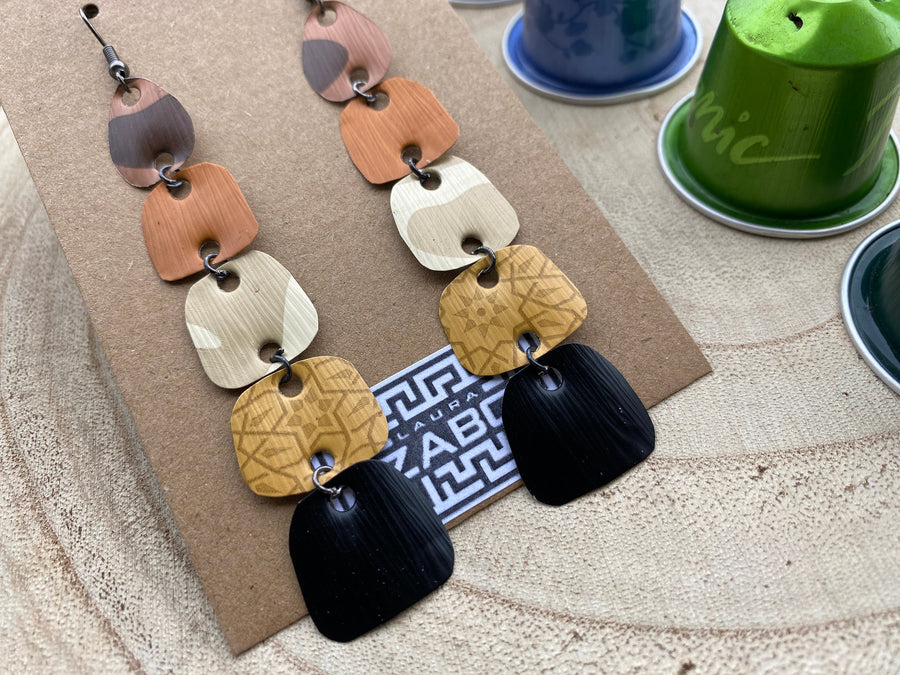 earthy coloured, brown black gold long earrings made from upcycled nespresso capsules on a wooden background, decorated with some whole nespresso capsules