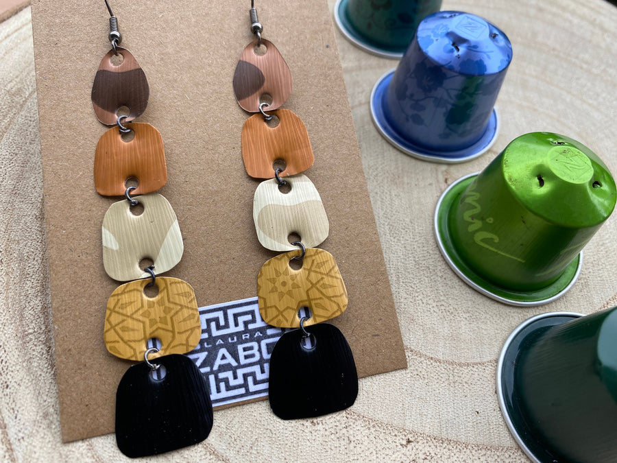 earthy coloured, brown black gold long earrings made from upcycled nespresso capsules on a wooden background, decorated with some whole nespresso capsules