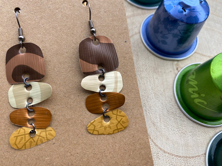 Earthy coloured, brown, sand mustard, gold earrings made from upcycled nespresso capsules on a wooden background with few whole nespresso pods