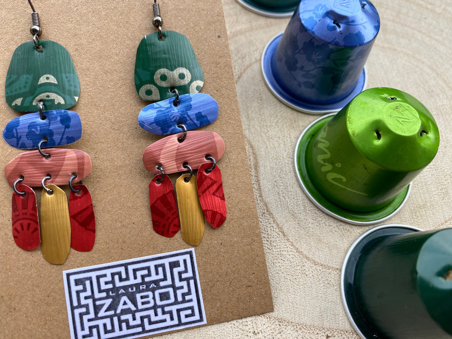 bright, colourful, green, blue, red, gold earrings made from recycled nespresso capsules on a wooden background and Laura Zabo logo and a few nespresso pods