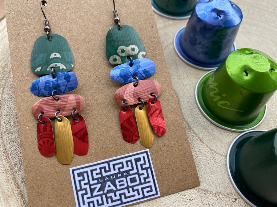 bright, colourful, green, blue, red, gold earrings made from recycled nespresso capsules on a wooden background and Laura Zabo logo and a few nespresso pods